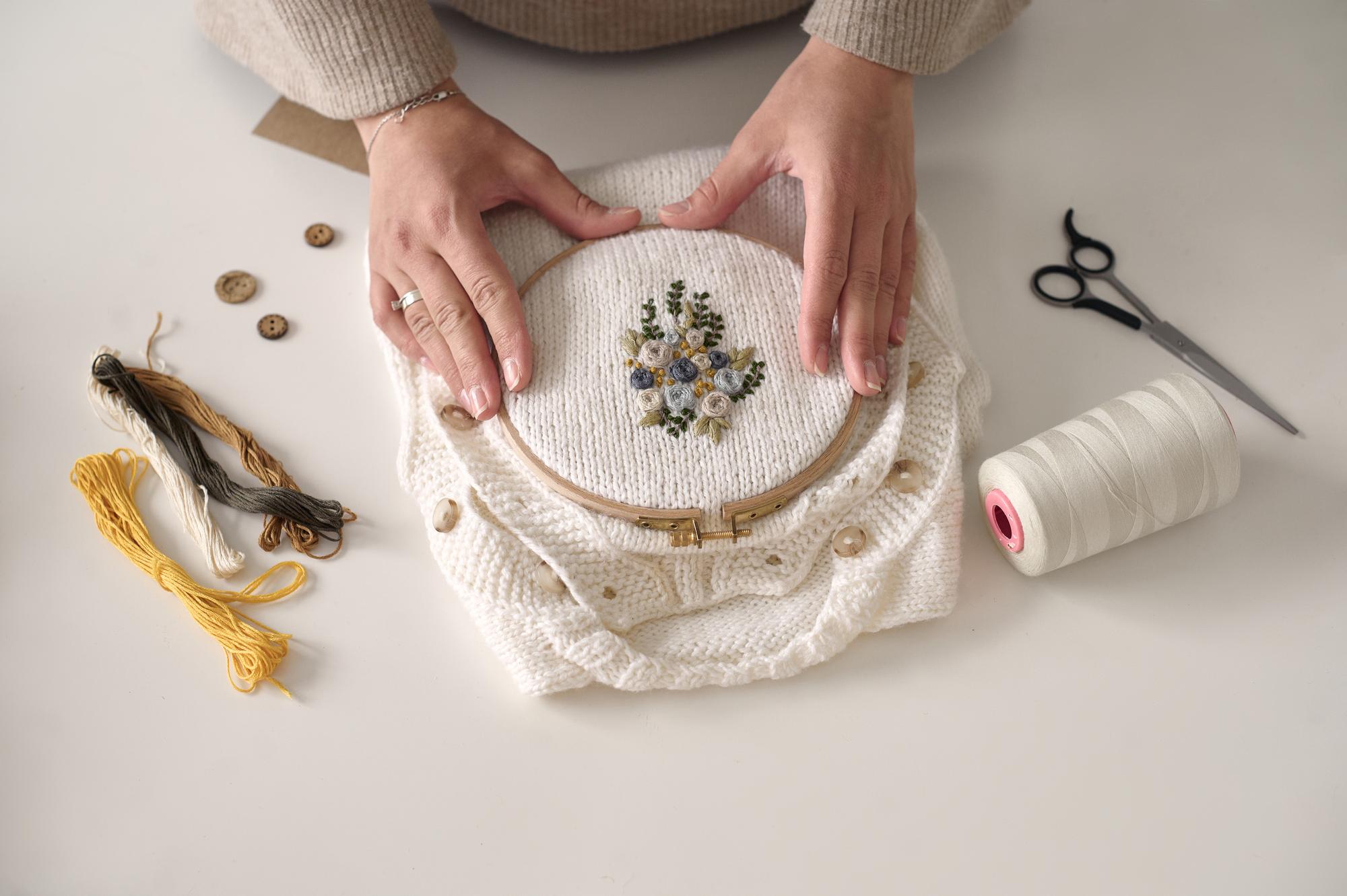 Close-up of hands embroidering floral pattern on linen